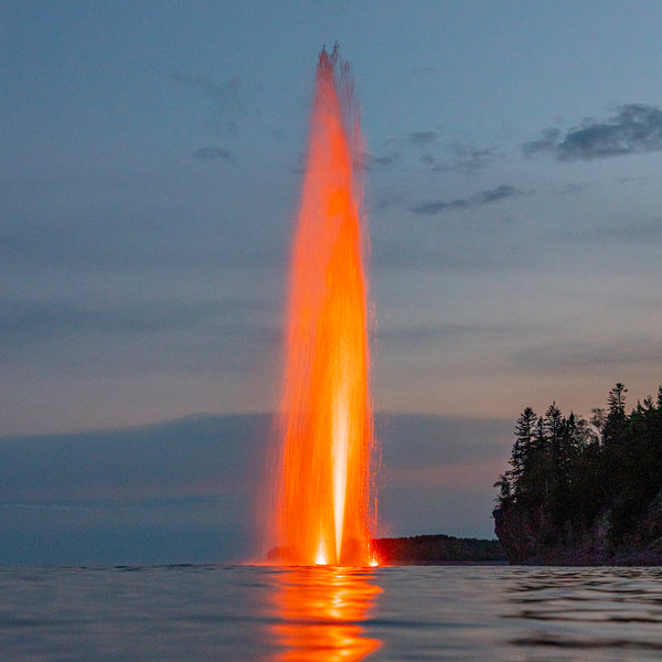 Red water fountain jet at dusk with trees in the background