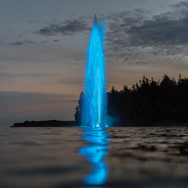 Blue water fountain at dusk with trees in the background